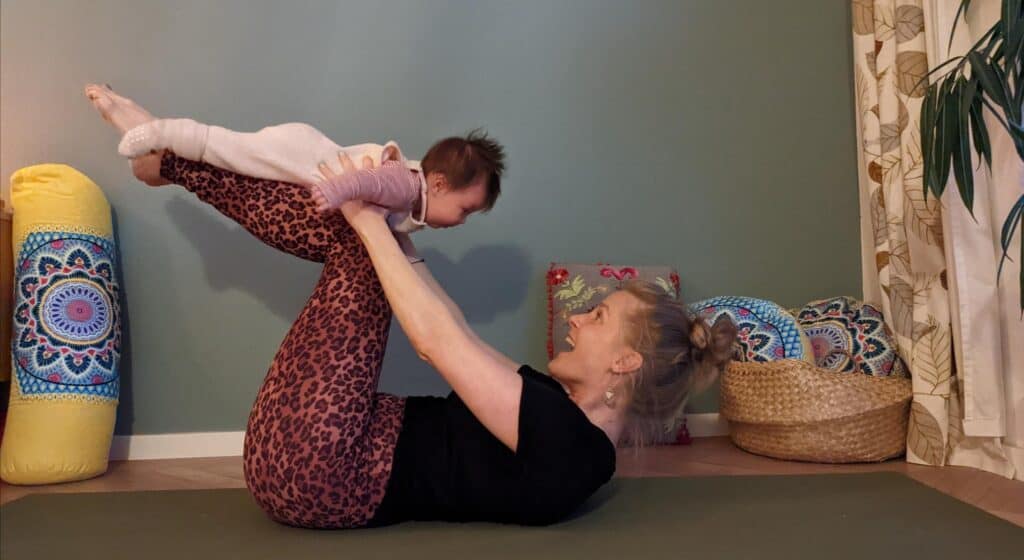 Mutter hält Baby beim Yoga im Familienbetrieb, entspannte Atmosphäre.
