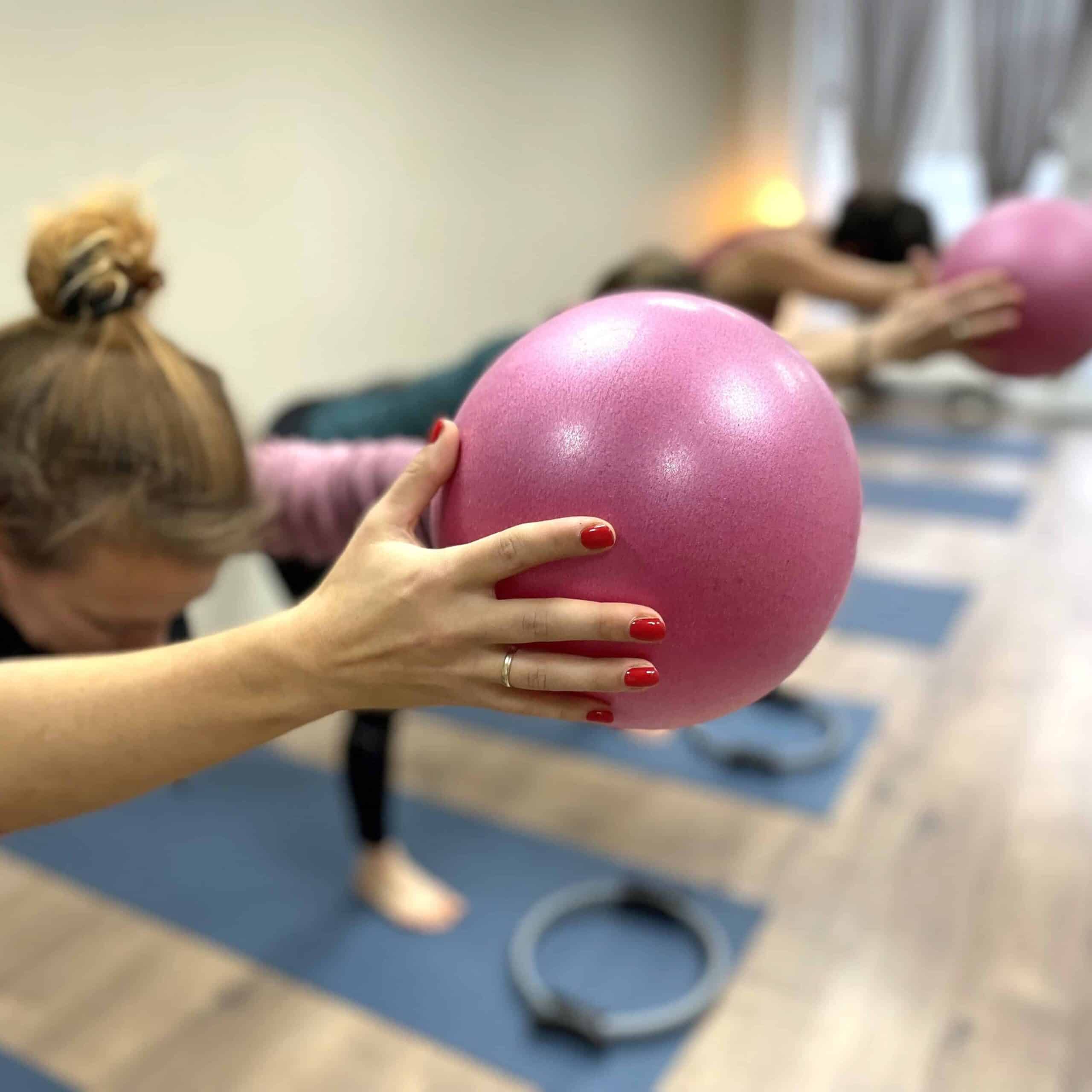 Frauen beim Fitnesskurs mit pinken Gymnastikbällen im Studio.